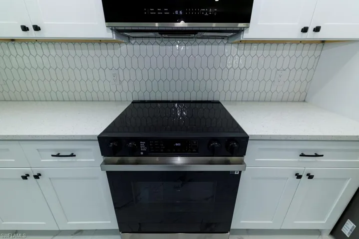 Kitchen featuring light stone countertops, electric range oven, white cabinetry, and tasteful backsplash