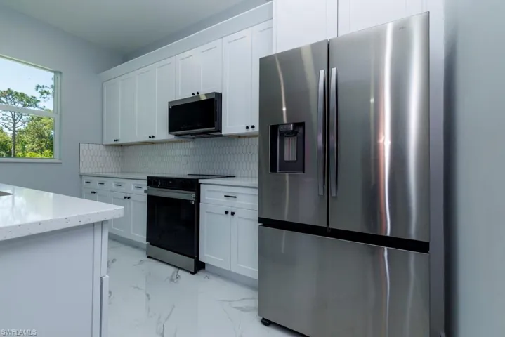 Kitchen with decorative backsplash, light stone counters, marble finish floor, stainless steel appliances, and white cabinetry