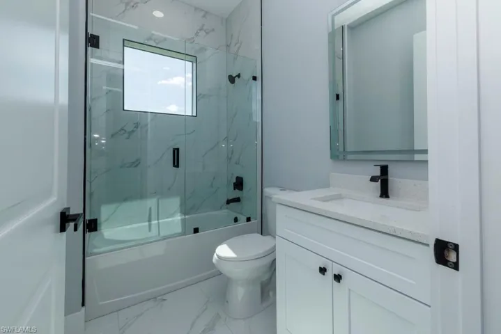 Full bath with vanity, marble finish floor, combined bath / shower with glass door, and toilet
