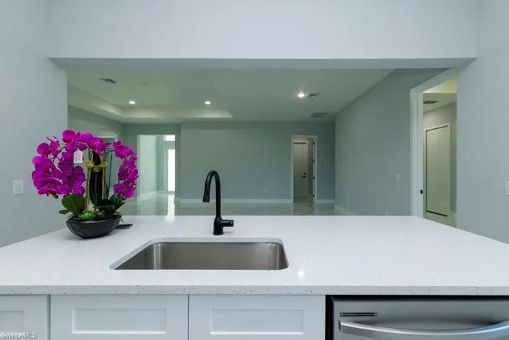Kitchen with stainless steel dishwasher, light stone countertops, recessed lighting, white cabinets, and a sink