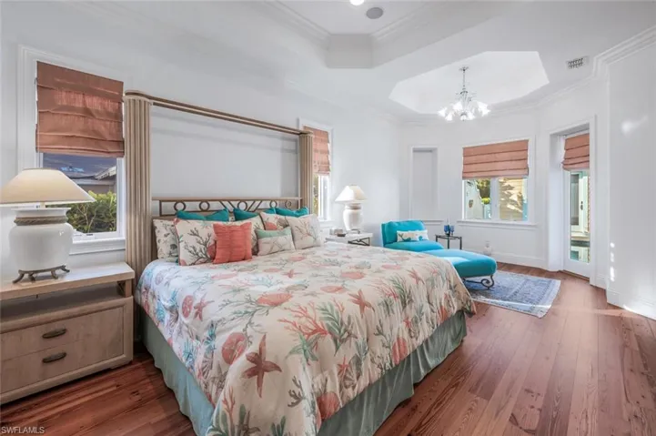 Bedroom featuring access to exterior, a tray ceiling, ornamental molding, dark hardwood / wood-style flooring, and a chandelier
