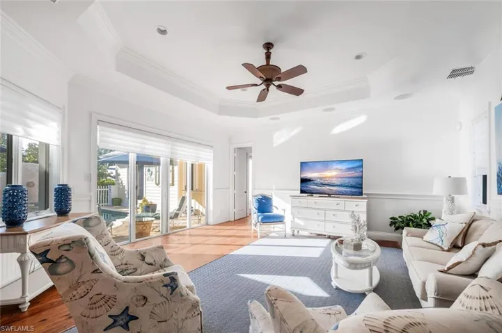 Living room featuring hardwood / wood-style flooring, ceiling fan, ornamental molding, and a raised ceiling