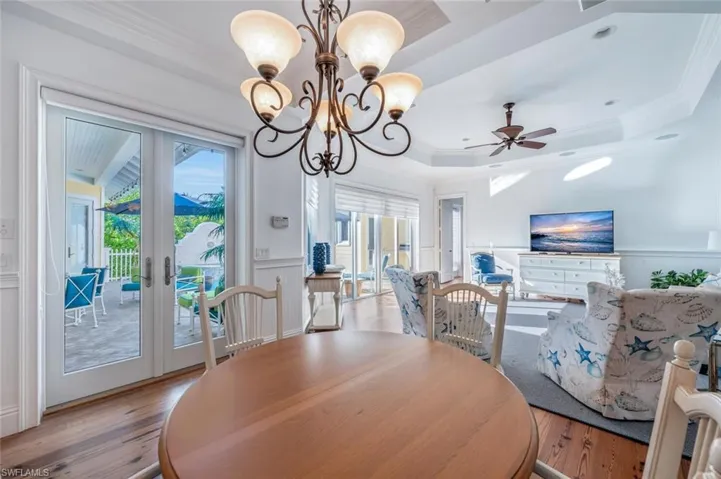 Dining area with ceiling fan with notable chandelier, a raised ceiling, crown molding, light wood-type flooring, and french doors