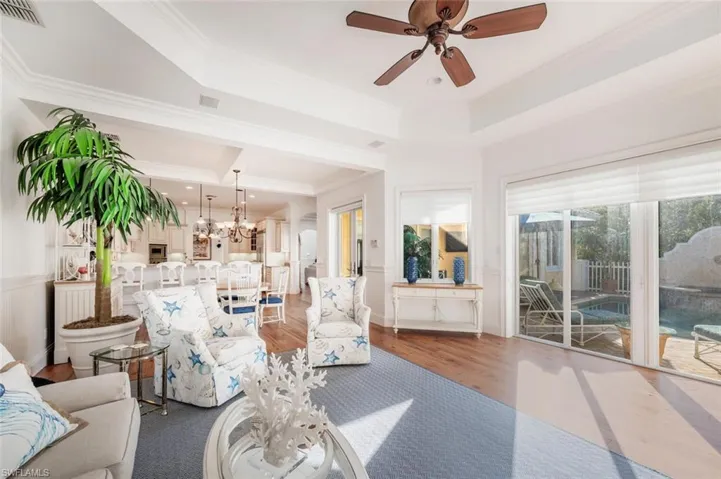 Living room with crown molding, a tray ceiling, ceiling fan with notable chandelier, and hardwood / wood-style flooring