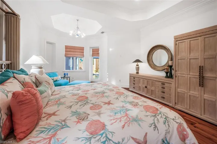 Bedroom with ornamental molding, hardwood / wood-style floors, a notable chandelier, and a tray ceiling