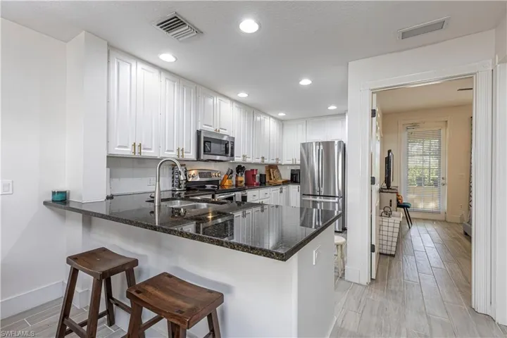 Kitchen with stainless steel appliances, a peninsula, a breakfast bar area, white cabinetry, and dark stone countertops
