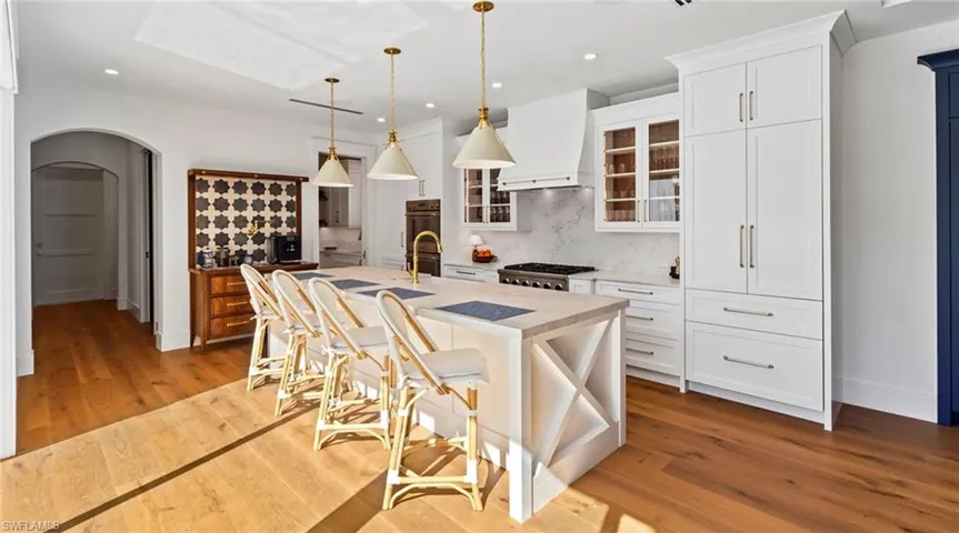 Kitchen with a breakfast bar area, arched walkways, pendant lighting, glass fronted cabinets, and an island with sink