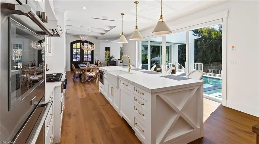 Kitchen featuring stainless steel appliances, a center island with sink, white cabinets, and dark wood finished floors