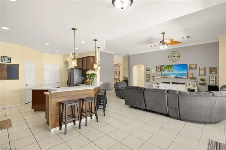 Living area featuring arched walkways, a ceiling fan, light tile patterned floors, ornamental molding, and baseboards