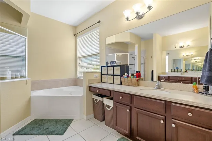 Full bath featuring a stall shower, tile patterned flooring, a garden tub, vanity, and baseboards