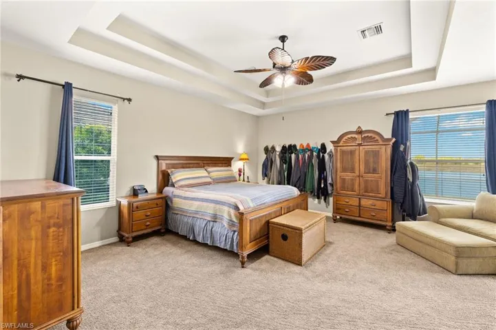 Bedroom featuring a tray ceiling, light colored carpet, ceiling fan, and baseboards