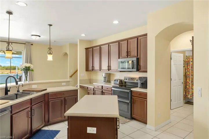 Kitchen featuring appliances with stainless steel finishes, a sink, arched walkways, pendant lighting, and light countertops