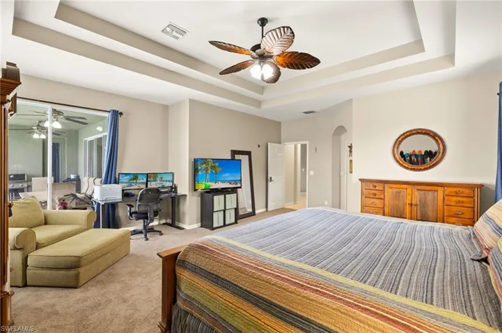 Carpeted bedroom with a tray ceiling, arched walkways, a desk, baseboards, and a ceiling fan