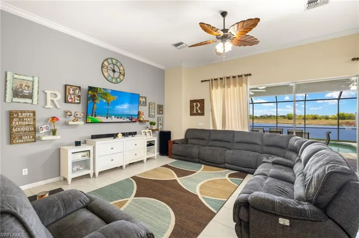 Living room with a ceiling fan, crown molding, baseboards, and light tile patterned flooring