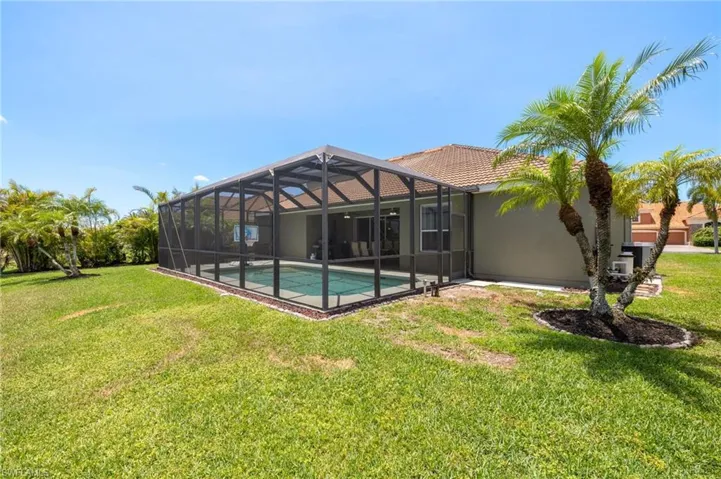 Rear view of house featuring a lawn, a tiled roof, an outdoor pool, stucco siding, and glass enclosure