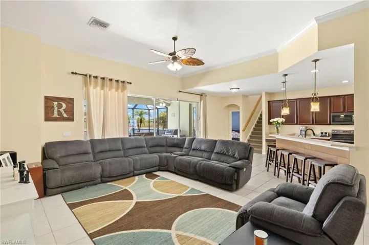 Living room with light tile patterned floors, ornamental molding, a ceiling fan, arched walkways, and stairs