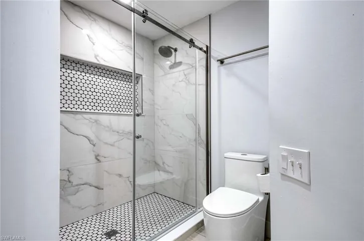 Full bath with a marble finish shower and toilet