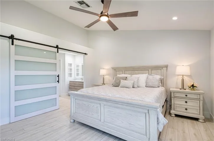 Bedroom featuring ensuite bathroom, light wood finished floors, a barn door, ceiling fan, and recessed lighting