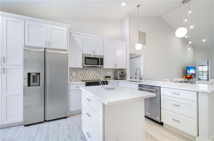 Kitchen featuring white cabinets, appliances with stainless steel finishes, decorative light fixtures, a center island, and a peninsula