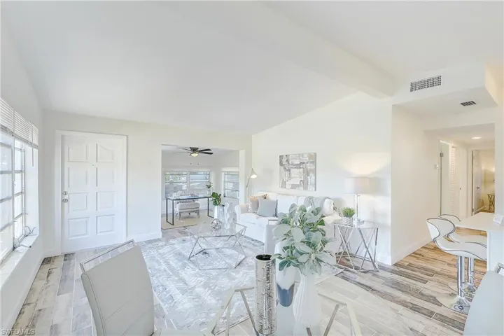 Living room featuring visible vents, baseboards, light wood-type flooring, and lofted ceiling with beams