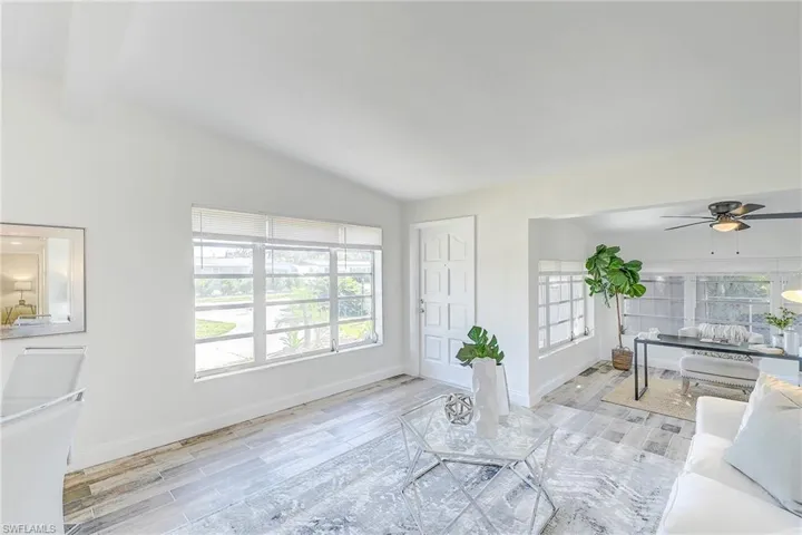 Living room featuring light wood-style floors, baseboards, a ceiling fan, and lofted ceiling with beams