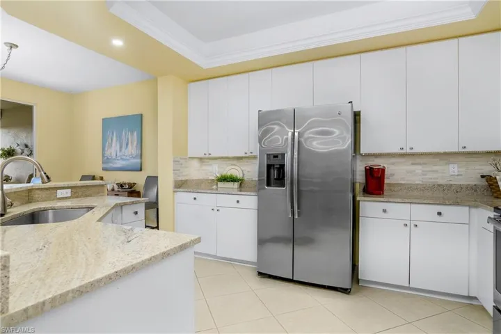 Kitchen featuring sink, stainless steel fridge with ice dispenser, light stone counters, and white cabinetry