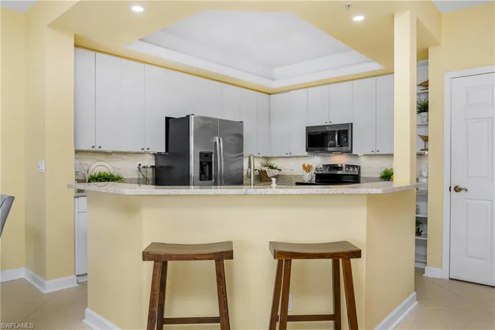 Kitchen featuring a kitchen breakfast bar, appliances with stainless steel finishes, a tray ceiling, and white cabinetry
