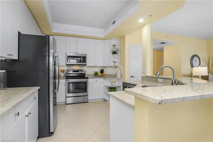 Kitchen featuring a raised ceiling, white cabinetry, light stone countertops, sink, and stainless steel appliances
