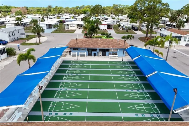 Outdoor shuffleboard courts with overhead sun shades and a building with a tiled roof