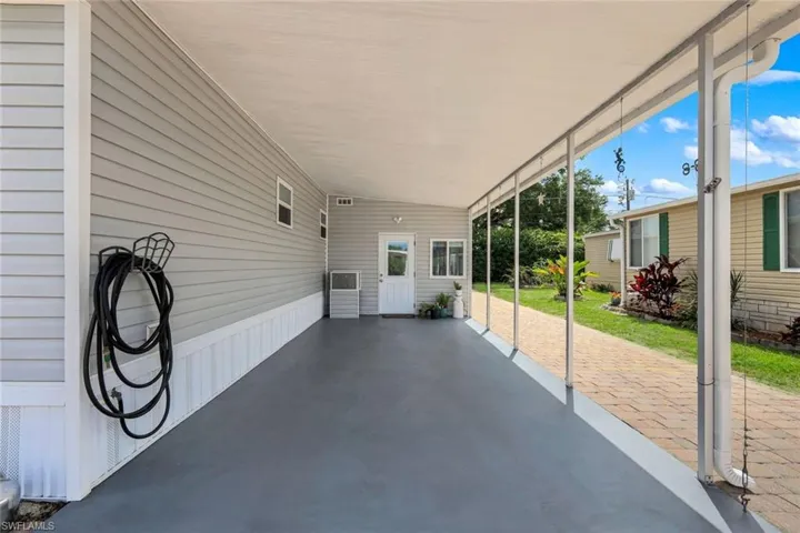 This property features a covered carport with a gray concrete floor and a white ceiling with extra parking on pavers