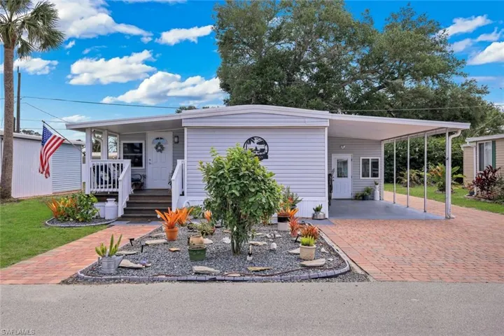 The property features a well-maintained exterior with light-colored siding, a covered entryway with steps, and a carport