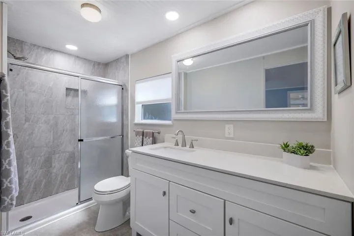Bathroom featuring a spacious shower with sliding glass doors and tiled walls, a vanity with a quartz countertop and basin sink, and an ornate framed mirror