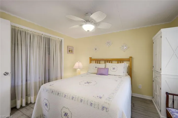 This room features light yellow walls, a ceiling fan with integrated lighting, and a window with sheer curtains