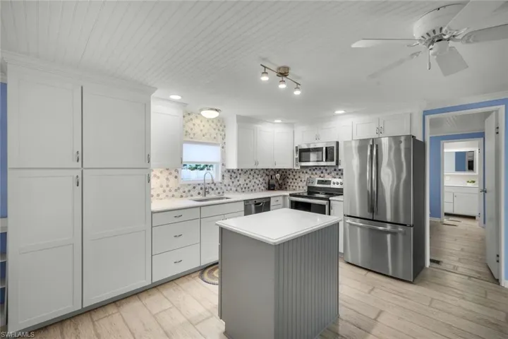 The kitchen features white cabinetry, stainless steel appliances, a center island with a white countertop, and laminate flooring