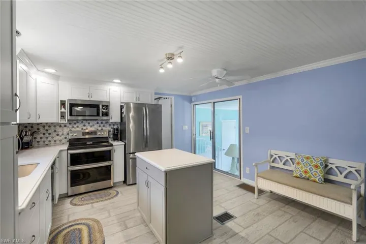 Kitchen featuring white cabinetry, stainless steel appliances, a center island with a quartz countertop, and laminate flooring