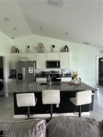 Kitchen featuring a vaulted ceiling with recessed lighting, granite countertops, white cabinetry, and stainless steel appliances