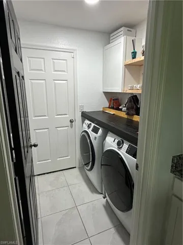 Dedicated laundry area featuring a dark wood-finish countertop, white cabinetry with integrated shelving, and light-toned tile flooring