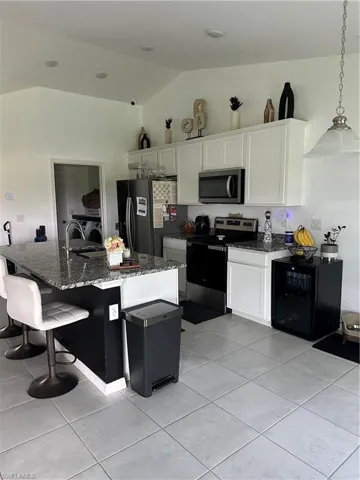 Kitchen featuring a granite-topped island with seating, stainless steel appliances, white cabinetry, and vaulted ceilings