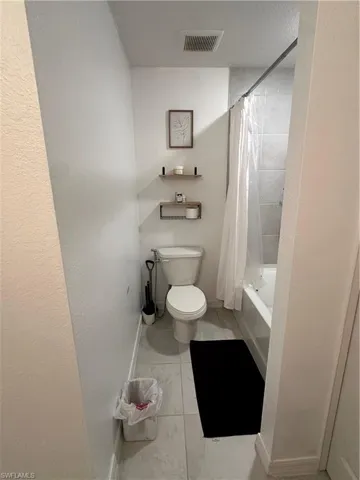Full bathroom featuring a white porcelain toilet, tiled flooring, built-in bathtub with tiled surround, and ceiling-mounted exhaust fan