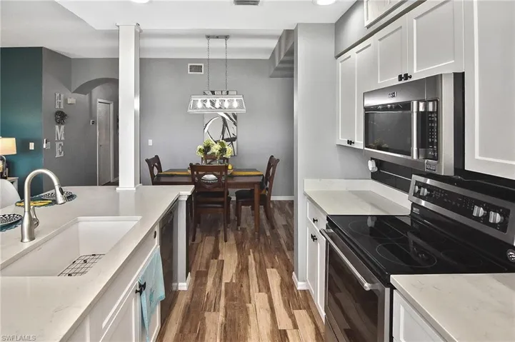 Kitchen with stainless steel appliances, dark wood-style flooring, white cabinets, and recessed lighting