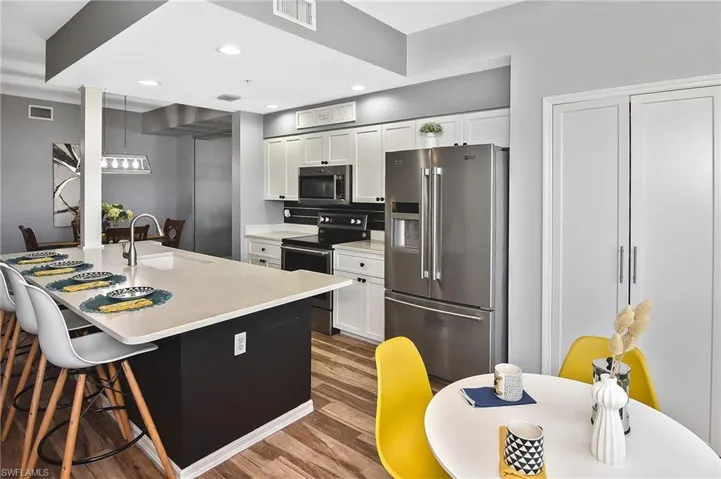 Kitchen with stainless steel appliances, white cabinets, a breakfast bar, light countertops, and light wood finished floors