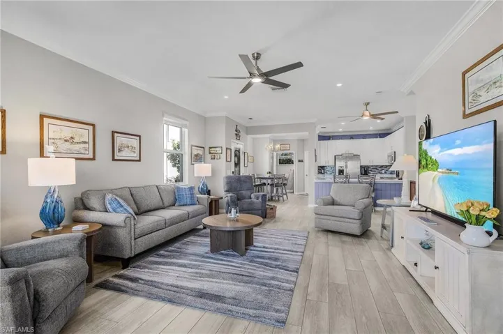 Living room with ornamental molding, recessed lighting, light wood-style flooring, and ceiling fan with notable chandelier