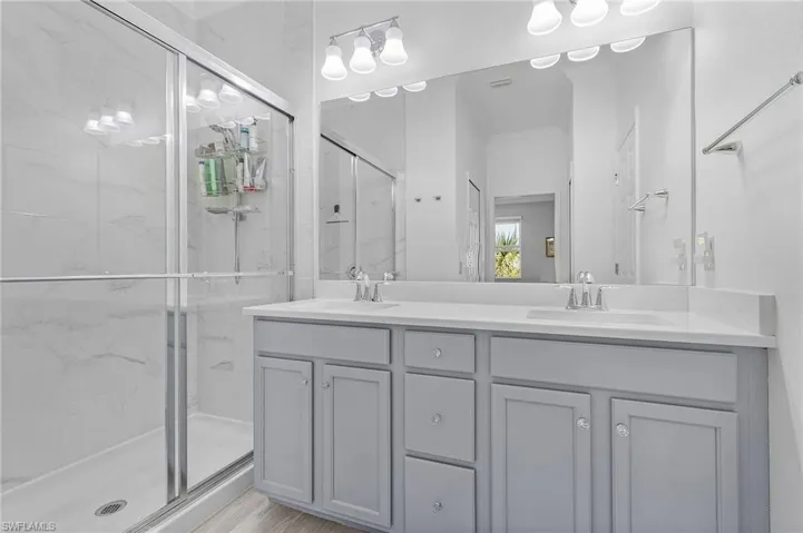 Full bath with double vanity, a marble finish shower, and a sink