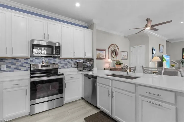 Kitchen with a sink, light countertops, appliances with stainless steel finishes, backsplash, and crown molding