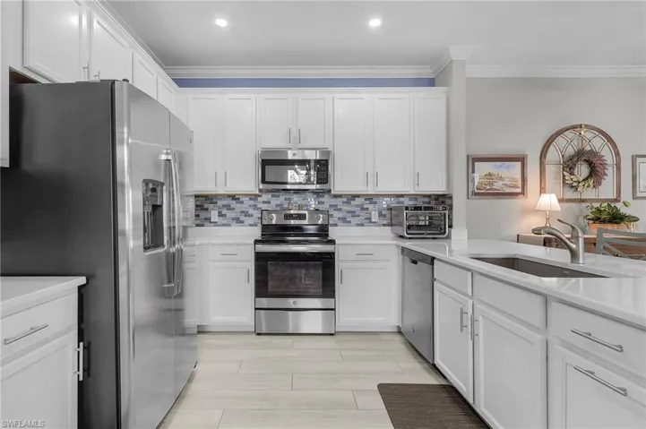 Kitchen featuring appliances with stainless steel finishes, white cabinetry, crown molding, and tasteful backsplash