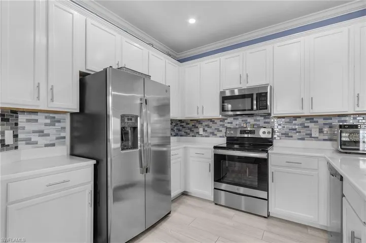 Kitchen featuring white cabinets, appliances with stainless steel finishes, light countertops, and backsplash