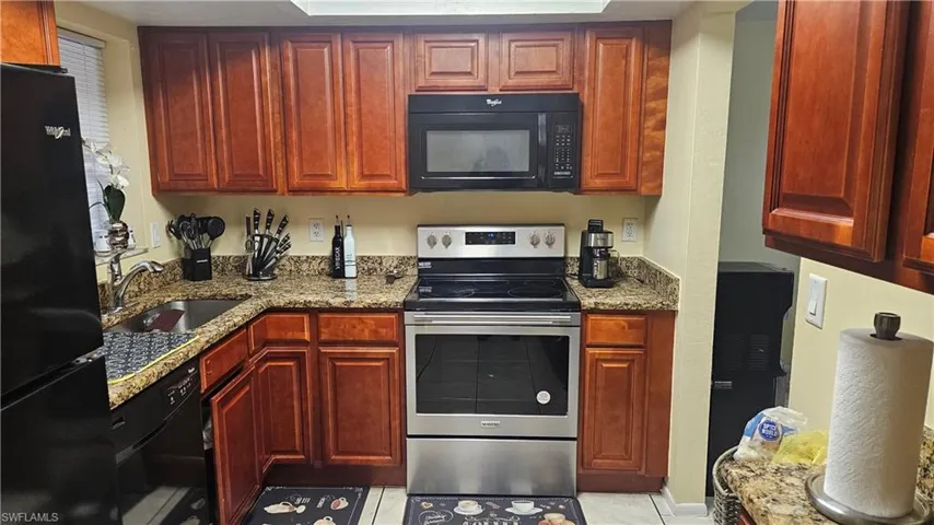 Kitchen with light tile patterned floors, sink, light stone countertops, and black appliances