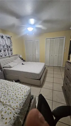 Bedroom with light tile patterned floors, ceiling fan, a textured ceiling, and two closets