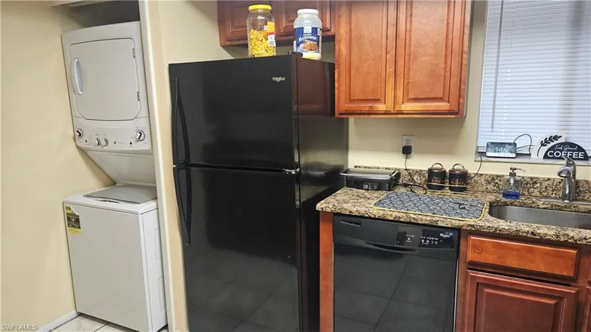 Kitchen featuring black appliances, sink, stacked washer / dryer, stone counters, and light tile patterned flooring