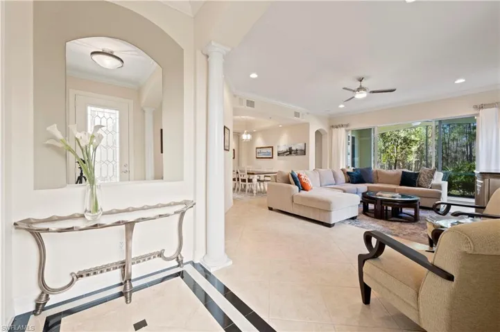Living area with arched walkways, crown molding, inlaid floor details, light tile patterned flooring, and ornate columns